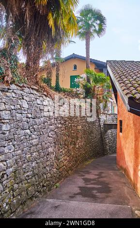 La vecchia strada di Castagnola con alte mura in pietra, che nasconde giardini verdi e case colorate, Lugano, Svizzera Foto Stock
