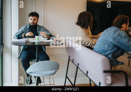 Tre professionisti si impegnano in un informale pranzo di lavoro in un moderno spazio ufficio, collaborando mentre si gusta un pasto. Foto Stock