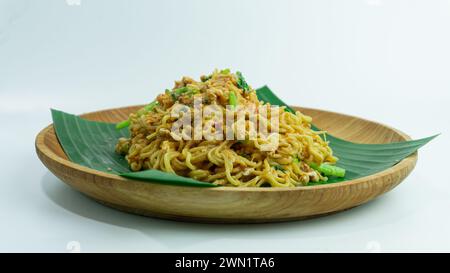 Mie Nyemek. Spaghetti fritti serviti su un piatto di legno ricoperto di foglie di banana, su sfondo bianco Foto Stock