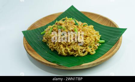 Mie Nyemek. Spaghetti fritti serviti su un piatto di legno ricoperto di foglie di banana, su sfondo bianco Foto Stock