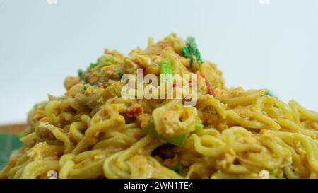 Mie Nyemek. Spaghetti fritti serviti su un piatto di legno ricoperto di foglie di banana, su sfondo bianco Foto Stock