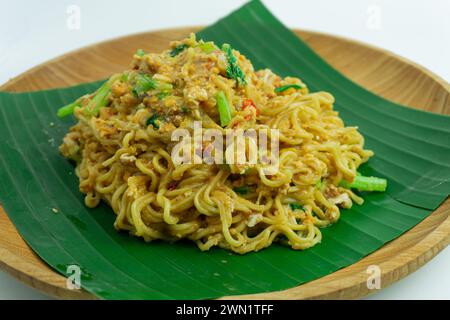 Mie Nyemek. Spaghetti fritti serviti su un piatto di legno ricoperto di foglie di banana, su sfondo bianco Foto Stock