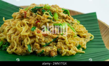 Mie Nyemek. Spaghetti fritti serviti su un piatto di legno ricoperto di foglie di banana, su sfondo bianco Foto Stock