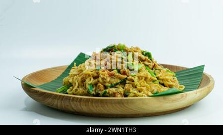 Mie Nyemek. Spaghetti fritti serviti su un piatto di legno ricoperto di foglie di banana, su sfondo bianco Foto Stock