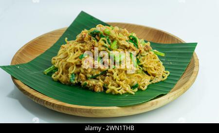 Mie Nyemek. Spaghetti fritti serviti su un piatto di legno ricoperto di foglie di banana, su sfondo bianco Foto Stock