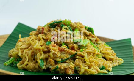 Mie Nyemek. Spaghetti fritti serviti su un piatto di legno ricoperto di foglie di banana, su sfondo bianco Foto Stock