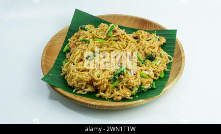 Mie Nyemek. Spaghetti fritti serviti su un piatto di legno ricoperto di foglie di banana, su sfondo bianco Foto Stock