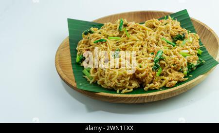 Mie Nyemek. Spaghetti fritti serviti su un piatto di legno ricoperto di foglie di banana, su sfondo bianco Foto Stock