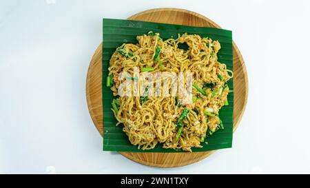 Mie Nyemek. Spaghetti fritti serviti su un piatto di legno ricoperto di foglie di banana, su sfondo bianco. Vista dall'alto Foto Stock