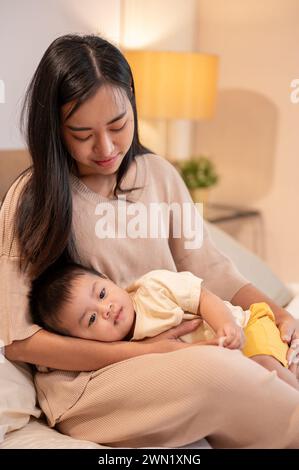 Una mamma asiatica premurosa sta mettendo il suo bambino a dormire tra le braccia. sonnaggio e ora di andare a letto, maternità e infanzia Foto Stock