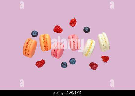 Macaron e bacche dolci volanti su sfondo lilla Foto Stock