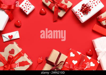 Cornice realizzata con bellissime confezioni regalo e caramelle su sfondo rosso. Festa di San Valentino Foto Stock