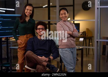 Gruppo di giovani sviluppatori etnicamente diversi che indossano eleganti abiti casual in posa per la fotocamera in un ufficio moderno Foto Stock