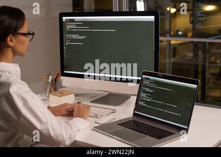 Giovane programmatrice moderna che sviluppa la digitazione del codice su un computer in ufficio moderno a tarda sera Foto Stock