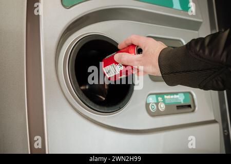 Restituzione di bottiglie e lattine vuote nella macchina di riciclaggio del supermercato per ridurre gli sprechi e riutilizzare plastica, vetro e alluminio. Mano che regge un barattolo Foto Stock