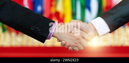 Uomini d'affari che stringono la mano davanti alle bandiere multinazionali Foto Stock
