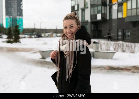 Una donna sorridente con dreadlock biondi cammina per la città con la neve in inverno Foto Stock