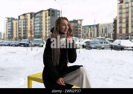 Una donna sorridente con dreadlock biondi cammina per la città con la neve in inverno Foto Stock