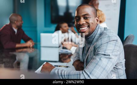 Un uomo d'affari professionista con una tuta elegante mostra fiducia con un sorriso caldo durante una riunione di gruppo in un set da ufficio moderno Foto Stock