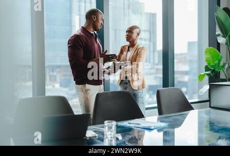 Due professionisti in una sala riunioni insieme, discutendo affari e pianificando affari aziendali. Il lavoro di squadra, la tecnologia e il successo sono evidenti Foto Stock