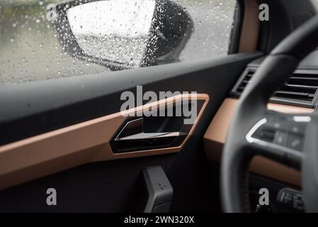 Guida in auto sotto la pioggia. Atmosfera intima e gocce di pioggia sulle vedove. Maniglia della portiera dell'auto ed elementi di rivestimento in rame. Foto Stock