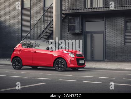 ed Citroen C1 di fronte all'edificio moderno. Vista anteriore di tre quarti della compatta berlina francese rossa in un ambiente urbano, parcheggiata sulla strada del centro Foto Stock