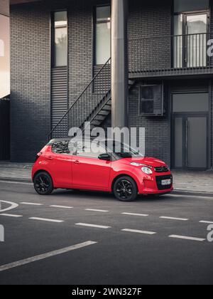 Citroen C1 di fronte ad un edificio moderno. Vista anteriore di tre quarti della compatta berlina francese rossa in un ambiente urbano, parcheggiata sulla strada in centro Foto Stock