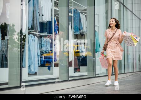 donna cammina attraverso affollato quartiere commerciale, tenendo borse di shopping pieno di abbigliamento alla moda Foto Stock