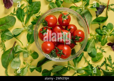 Vista dall'alto dei pomodori ciliegini, circondati da foglie verdi fresche su un tavolo. Ingredienti sani possono essere utilizzati in varie ricette alimentari naturali Foto Stock