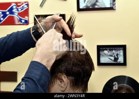 Il parrucchiere tiene in mano una ciocca di capelli dalla testa di una donna e la taglia con le forbici. Foto Stock