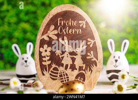 Augusta, Baviera, Germania - 28 febbraio 2024: Felice saluto pasquale su un uovo di Pasqua di legno accanto alla decorazione pasquale *** Frohe Ostern Gruß auf einem Osterei aus Holz neben Osterdekoration Foto Stock