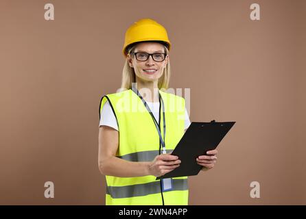 Ingegnere in elmetto che tiene appunti su sfondo marrone Foto Stock