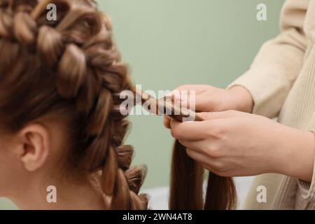 Stilista professionista che intreccia i capelli di donna su sfondo color oliva, primo piano Foto Stock