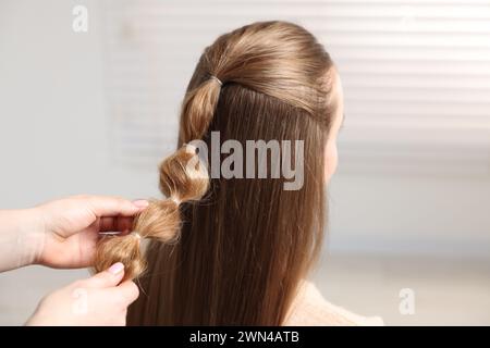 Stilista professionista che intreccia i capelli di donna in casa, primo piano Foto Stock