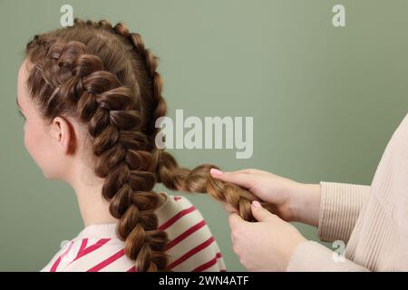 Stilista professionista che intreccia i capelli di donna su sfondo color oliva, primo piano Foto Stock