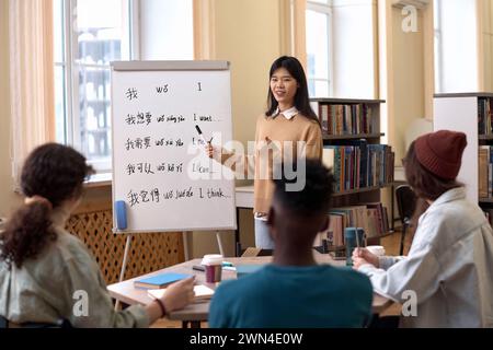 Ritratto di una giovane donna asiatica che insegna lezioni di lingua cinese a un gruppo di studenti e che indica i geroglifici sulla lavagna Foto Stock