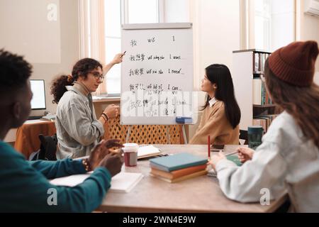 Vista laterale ritratto di uno studente di sesso maschile che risponde alle domande durante la lezione di lingua cinese e che indica la lavagna con geroglifici Foto Stock
