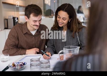 Coppia felice sorridente mentre firma un accordo alla scrivania dell'ufficio immobiliare Foto Stock