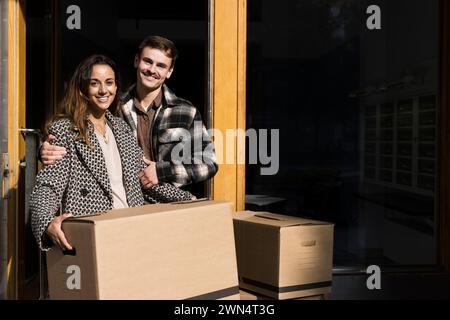 Ritratto di un uomo sorridente che abbraccia una donna che tiene una scatola di cartone davanti all'appartamento Foto Stock