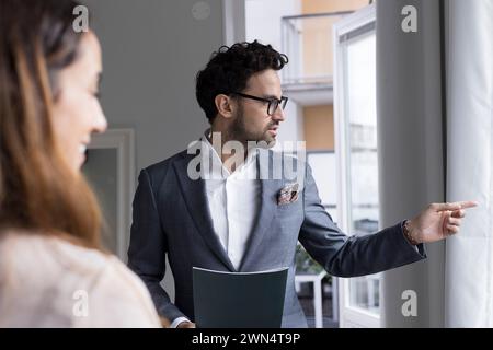 Agente immobiliare maschio che indica mentre parla con una cliente donna a casa Foto Stock