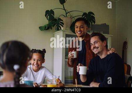 Felice coppia gay che parla con le figlie mentre fa colazione a casa Foto Stock