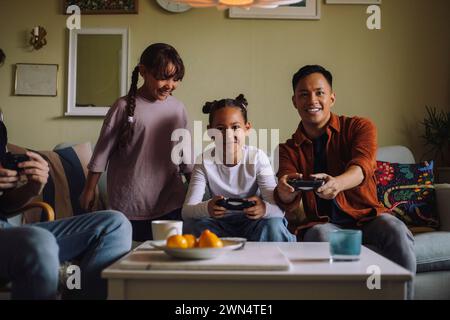 Ritratto di coppia gay felice che gioca a videogame con la figlia seduto sul divano a casa Foto Stock