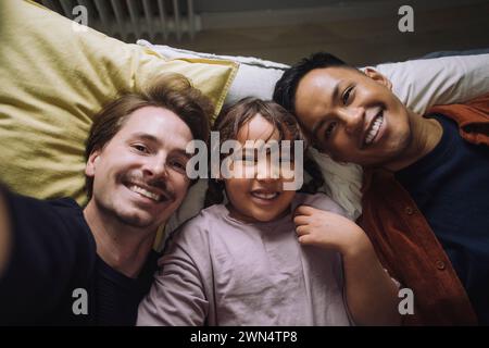Direttamente sopra il ritratto di una coppia gay felice sdraiata con la figlia a casa Foto Stock