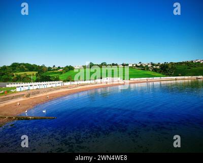 Una foto aerea con drone della spiaggia di Goodrington Sands Paignton Devon UK con una lunga fila di capanne vicino alla spiaggia sabbiosa e al mare e al cielo calmi e blu Foto Stock