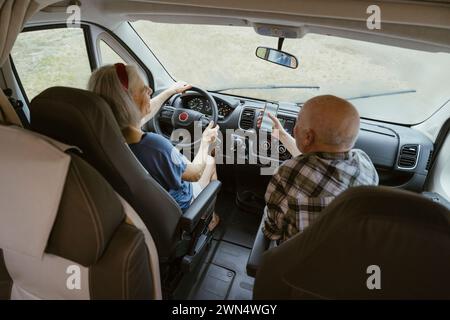 Uomo anziano che condivide lo smartphone con una donna che guida un camper durante il viaggio Foto Stock