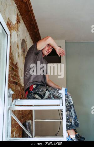 Lavoratore sorridente seduto sulla scala in pausa sul posto Foto Stock