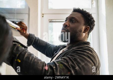 Giovane carpentiere maschio armadietto di misurazione in cucina nell'appartamento Foto Stock