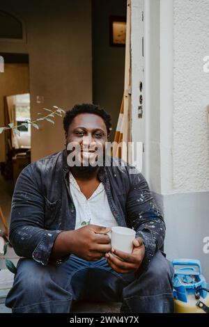 Ritratto di un falegname sorridente che tiene in mano un caffè all'ingresso della casa Foto Stock