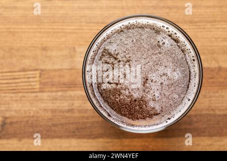 Vista dall'alto verso il basso di una birra artigianale appena versata in un bicchiere posto su un tavolo in legno dai toni caldi Foto Stock