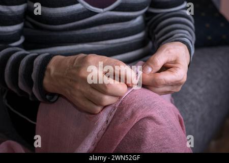 Le mani di una donna anziana cucono sciarpa rosa Foto Stock